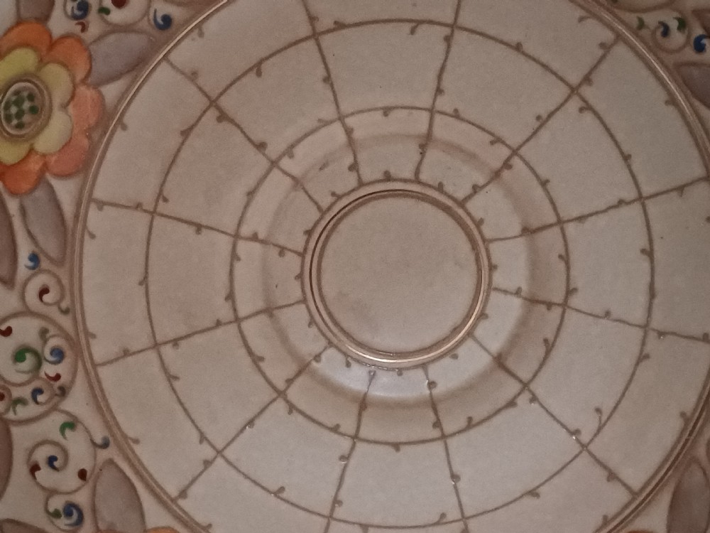 A round Art Deco earthenware bowl featuring a central circular spider-web trellis design surrounded by tube-lined floral motifs in orange and beige. View VI