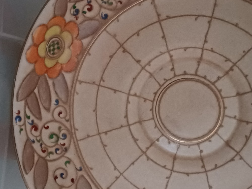 A round Art Deco earthenware bowl featuring a central circular spider-web trellis design surrounded by tube-lined floral motifs in orange and beige. View VII