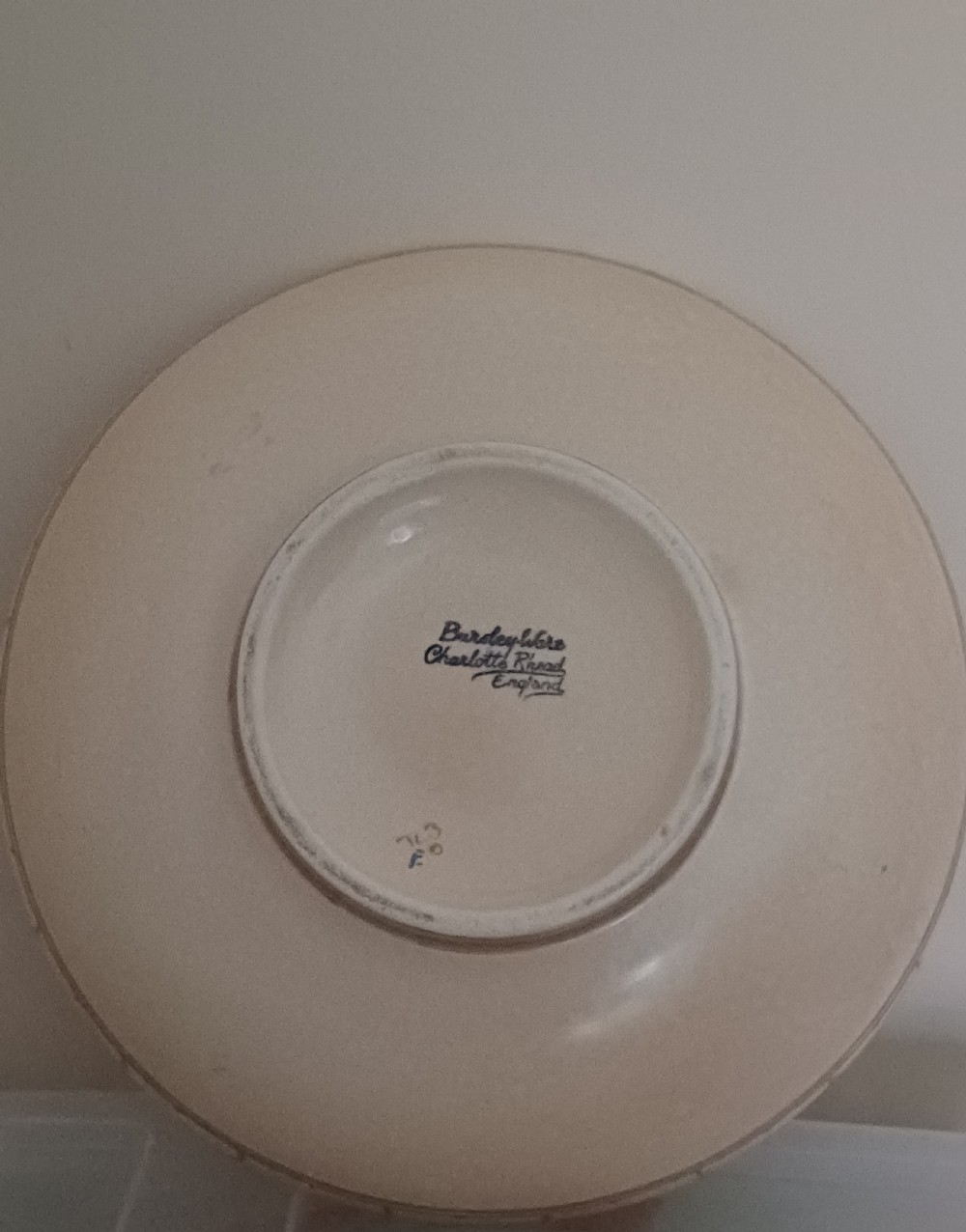 A round Art Deco earthenware bowl featuring a central circular spider-web trellis design surrounded by tube-lined floral motifs in orange and beige. View X