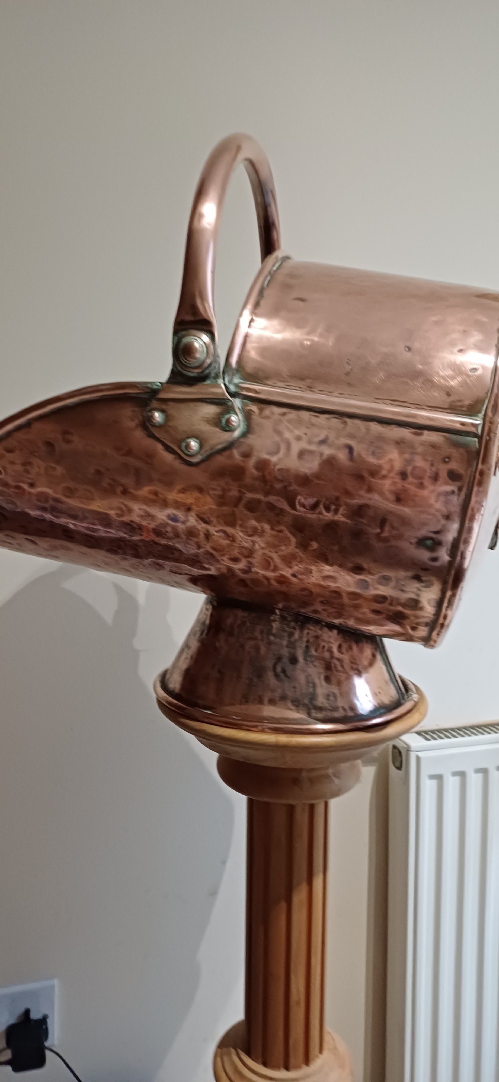 A hand-hammered copper helmet-shaped coal scuttle featuring a curved handle, riveted mountings, and a flared pedestal base. View IX