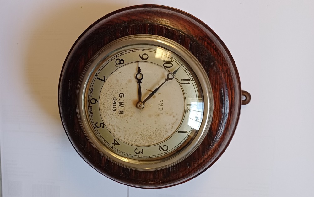 A circular dark oak GWR signal box clock featuring a brass bezel, glass face cover, cream dial with Arabic numerals, and black clock hands. View X