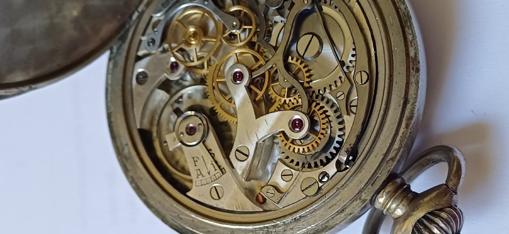 An open-face pocket watch featuring a black dial, luminescent white Arabic numerals, two sub-dials, and a silver-coloured metal case with an onion crown. View X