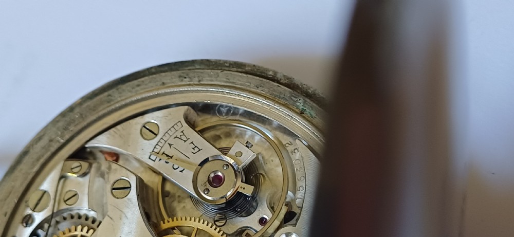 An open-face pocket watch featuring a black dial, luminescent white Arabic numerals, two sub-dials, and a silver-coloured metal case with an onion crown. View XII