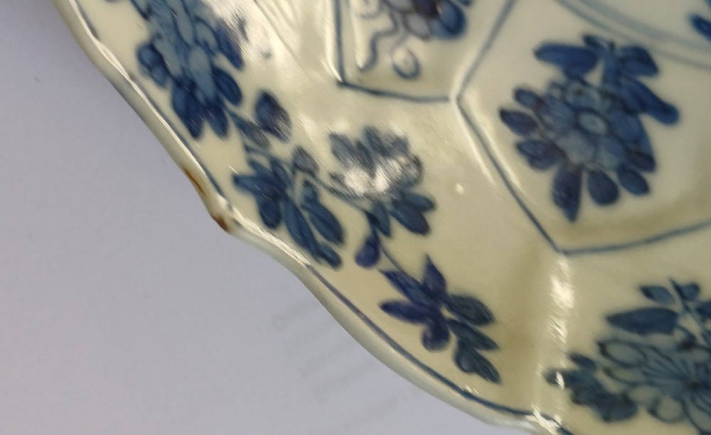 A circular Chinese porcelain dish painted with blue cobalt floral motifs, featuring a barbed rim and radiating moulded petal panels. View IX