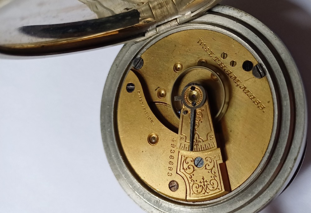 An open-face antique pocket watch featuring a silver-coloured metal casing, cream enamel dial with black Roman numerals, and a gold-toned winding crown. View XIII