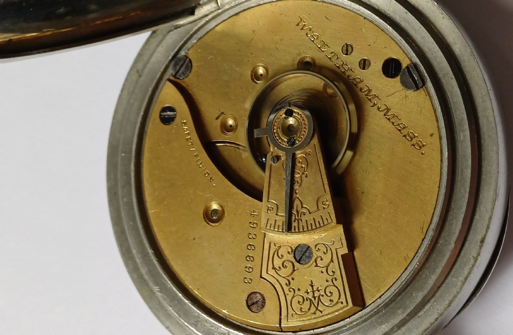 An open-face antique pocket watch featuring a silver-coloured metal casing, cream enamel dial with black Roman numerals, and a gold-toned winding crown. View XV