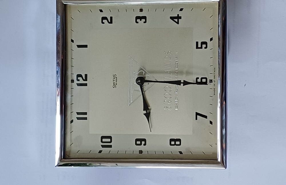 A square mid-century chrome desk clock featuring a cream dial with black Arabic numerals and embossed Alvis and Brooklands branding. View II