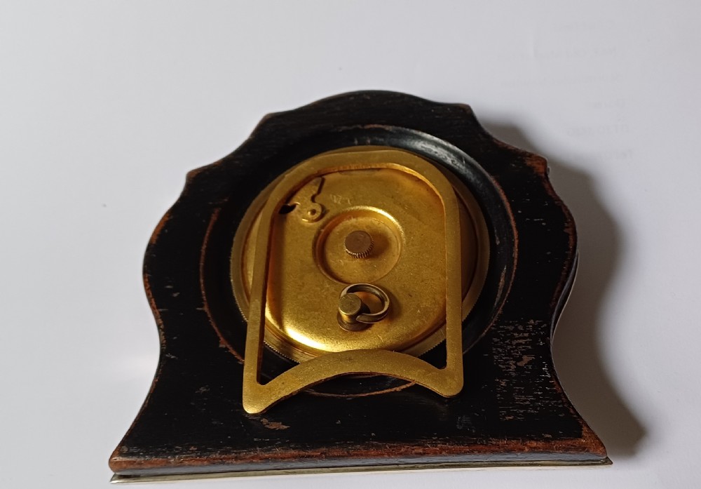 An Art Deco engine-turned silver strut desk clock featuring a shaped outline, circular dial with Arabic numerals, and an engraved circular plaque dated 1927. View XII