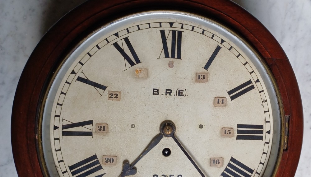 An early 20th-century round mahogany railway wall clock featuring an off-white dial with Roman numerals, secondary 24-hour markings, and B.R.(E.) lettering. View VI