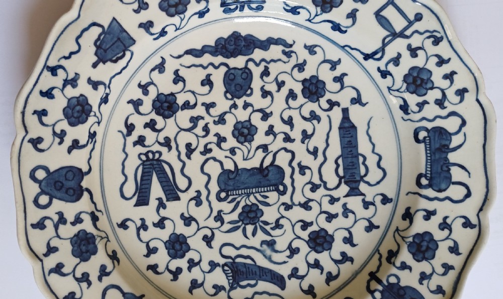 An 18th-century circular soft-paste porcelain plate with a scalloped rim, featuring underglaze cobalt blue Chinese-inspired motifs and scrolling foliage. View III