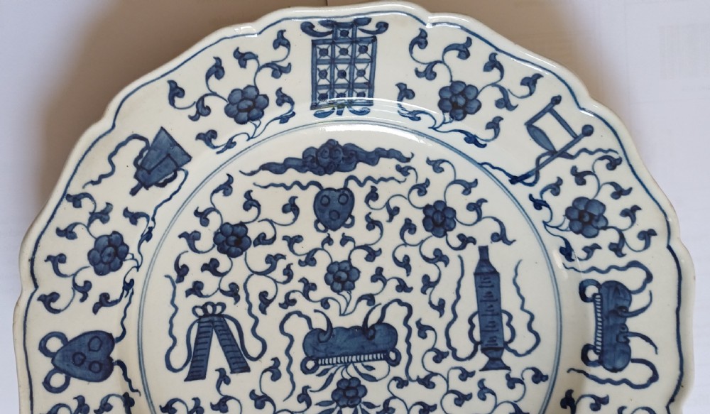 An 18th-century circular soft-paste porcelain plate with a scalloped rim, featuring underglaze cobalt blue Chinese-inspired motifs and scrolling foliage. View IV
