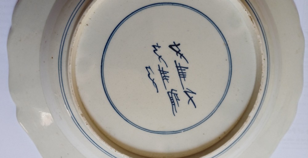 An 18th-century circular soft-paste porcelain plate with a scalloped rim, featuring underglaze cobalt blue Chinese-inspired motifs and scrolling foliage. View VI