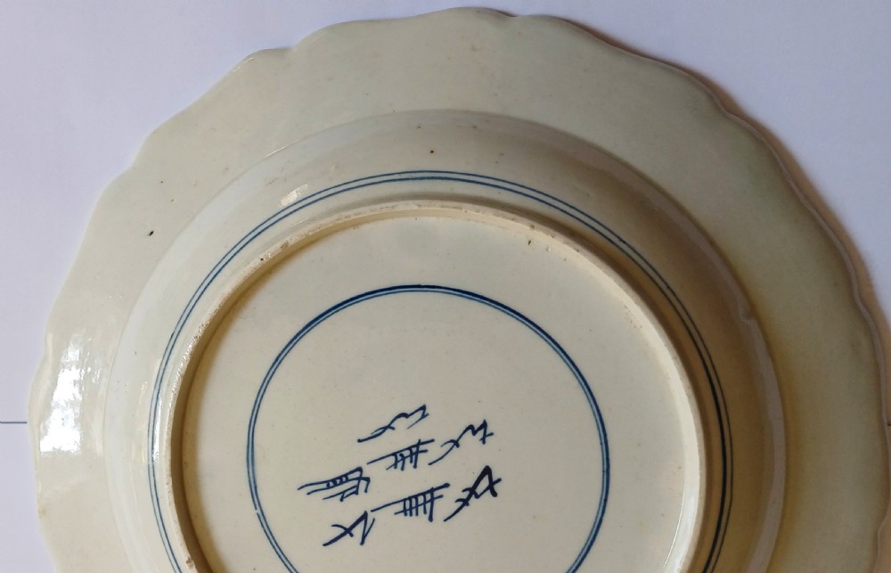 An 18th-century circular soft-paste porcelain plate with a scalloped rim, featuring underglaze cobalt blue Chinese-inspired motifs and scrolling foliage. View VII