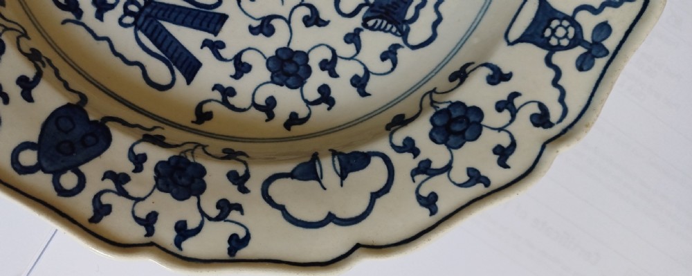 An 18th-century circular soft-paste porcelain plate with a scalloped rim, featuring underglaze cobalt blue Chinese-inspired motifs and scrolling foliage. View XI