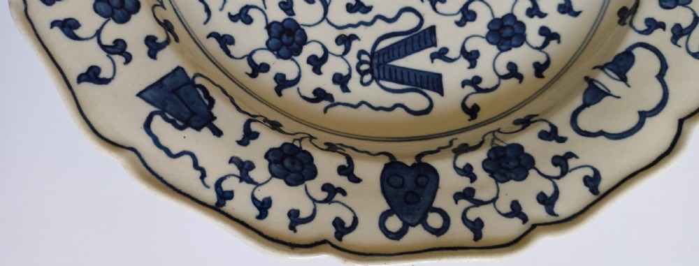 An 18th-century circular soft-paste porcelain plate with a scalloped rim, featuring underglaze cobalt blue Chinese-inspired motifs and scrolling foliage. View XII