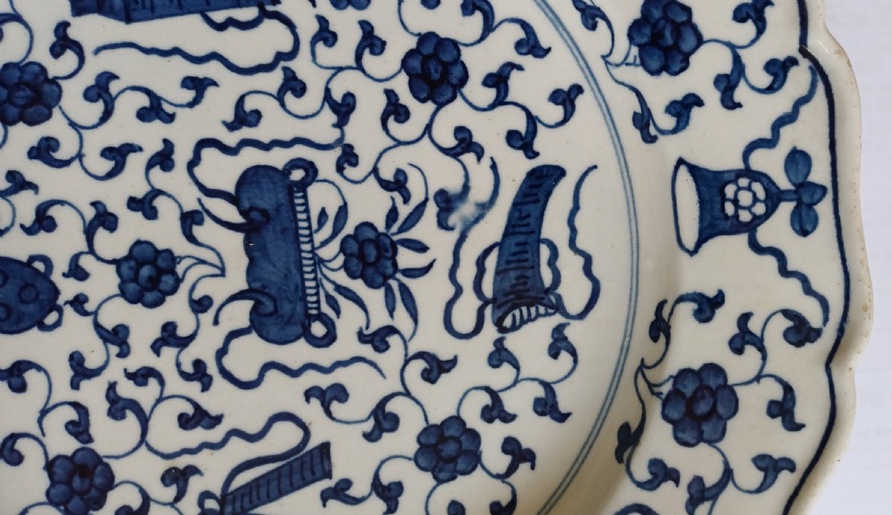 An 18th-century circular soft-paste porcelain plate with a scalloped rim, featuring underglaze cobalt blue Chinese-inspired motifs and scrolling foliage. View XIII