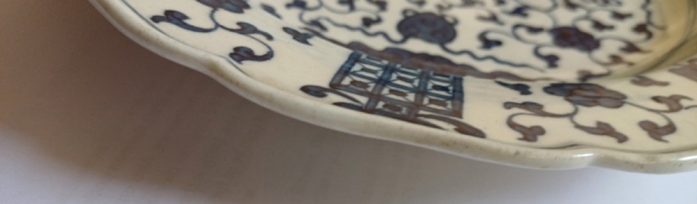 An 18th-century circular soft-paste porcelain plate with a scalloped rim, featuring underglaze cobalt blue Chinese-inspired motifs and scrolling foliage. View XV