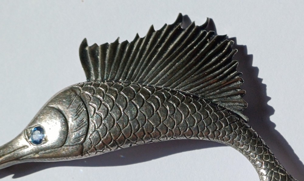 A vintage silver brooch shaped as a sailfish with detailed scales, a prominent ribbed dorsal fin, and a light blue stone set in the eye. View III