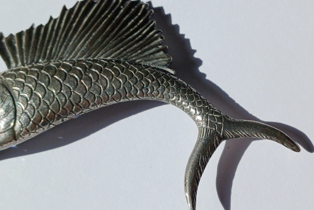 A vintage silver brooch shaped as a sailfish with detailed scales, a prominent ribbed dorsal fin, and a light blue stone set in the eye. View IV
