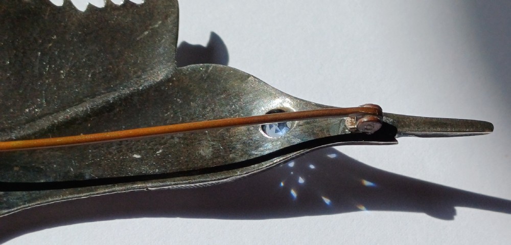 A vintage silver brooch shaped as a sailfish with detailed scales, a prominent ribbed dorsal fin, and a light blue stone set in the eye. View V