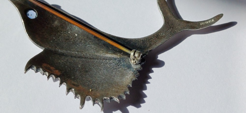 A vintage silver brooch shaped as a sailfish with detailed scales, a prominent ribbed dorsal fin, and a light blue stone set in the eye. View VII