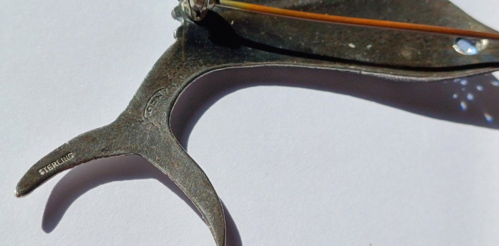 A vintage silver brooch shaped as a sailfish with detailed scales, a prominent ribbed dorsal fin, and a light blue stone set in the eye. View VIII