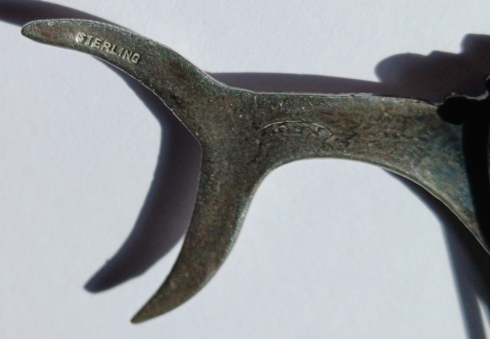 A vintage silver brooch shaped as a sailfish with detailed scales, a prominent ribbed dorsal fin, and a light blue stone set in the eye. View X