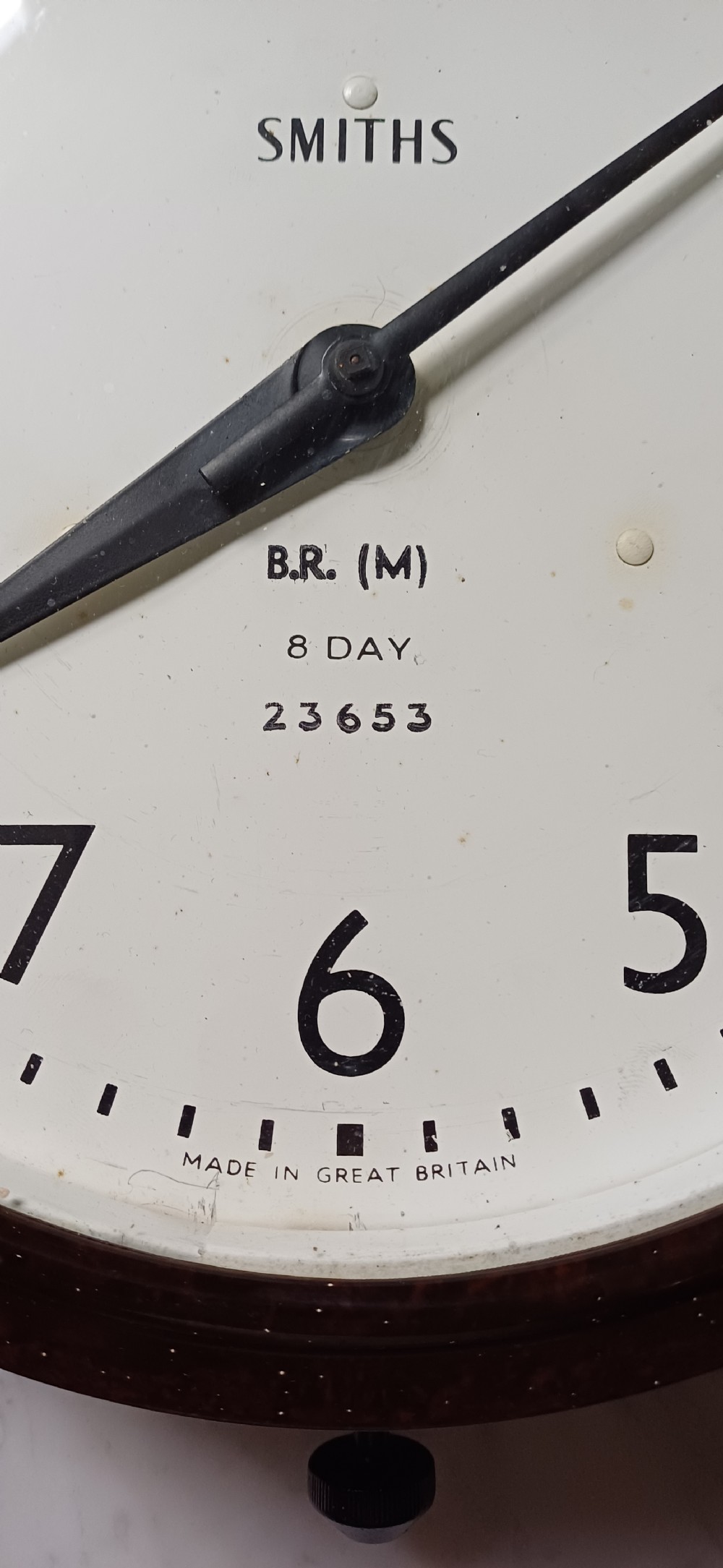A circular mid-century wall clock featuring a moulded dark brown Bakelite case, a white dial with black Arabic numerals, and dark hands. View III