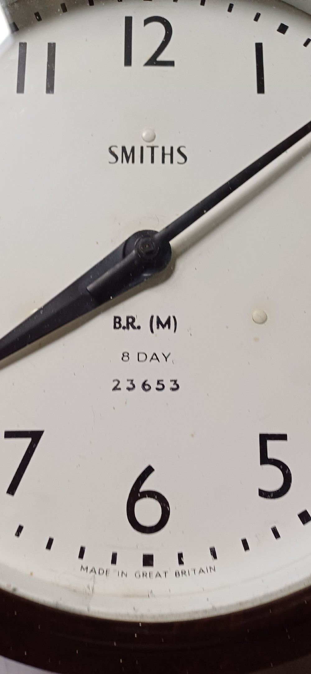 A circular mid-century wall clock featuring a moulded dark brown Bakelite case, a white dial with black Arabic numerals, and dark hands. View IV