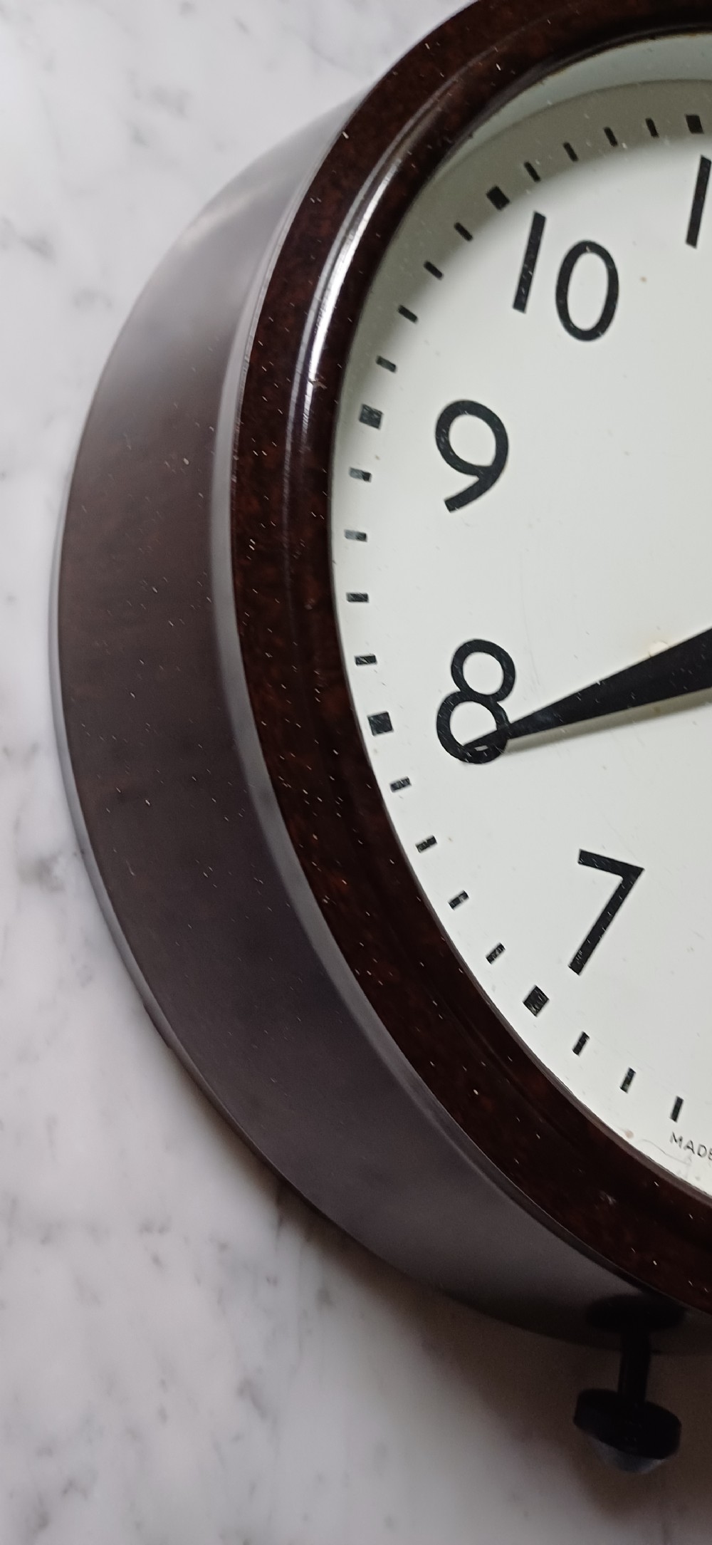 A circular mid-century wall clock featuring a moulded dark brown Bakelite case, a white dial with black Arabic numerals, and dark hands. View VI