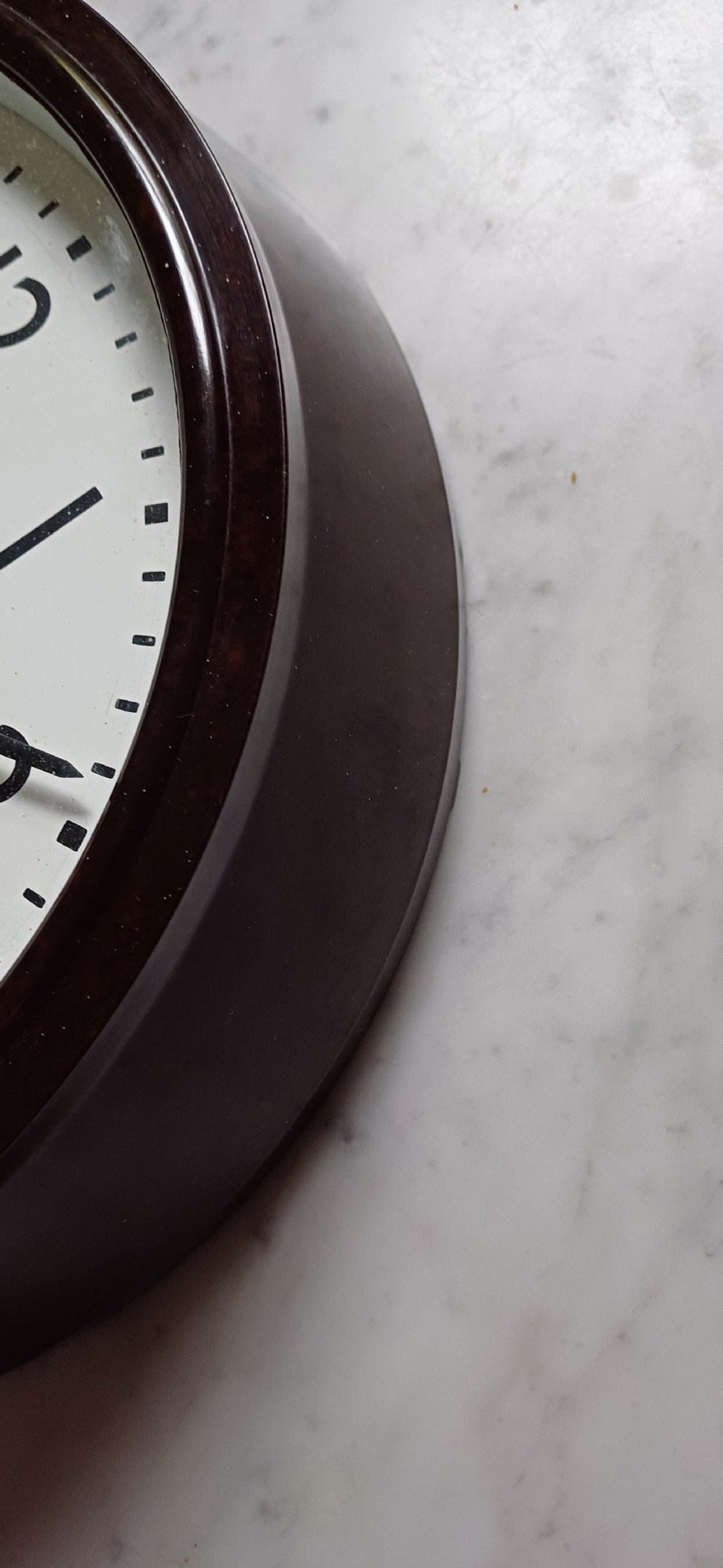 A circular mid-century wall clock featuring a moulded dark brown Bakelite case, a white dial with black Arabic numerals, and dark hands. View X