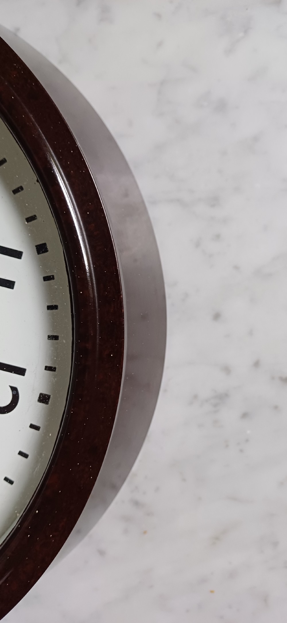 A circular mid-century wall clock featuring a moulded dark brown Bakelite case, a white dial with black Arabic numerals, and dark hands. View XII