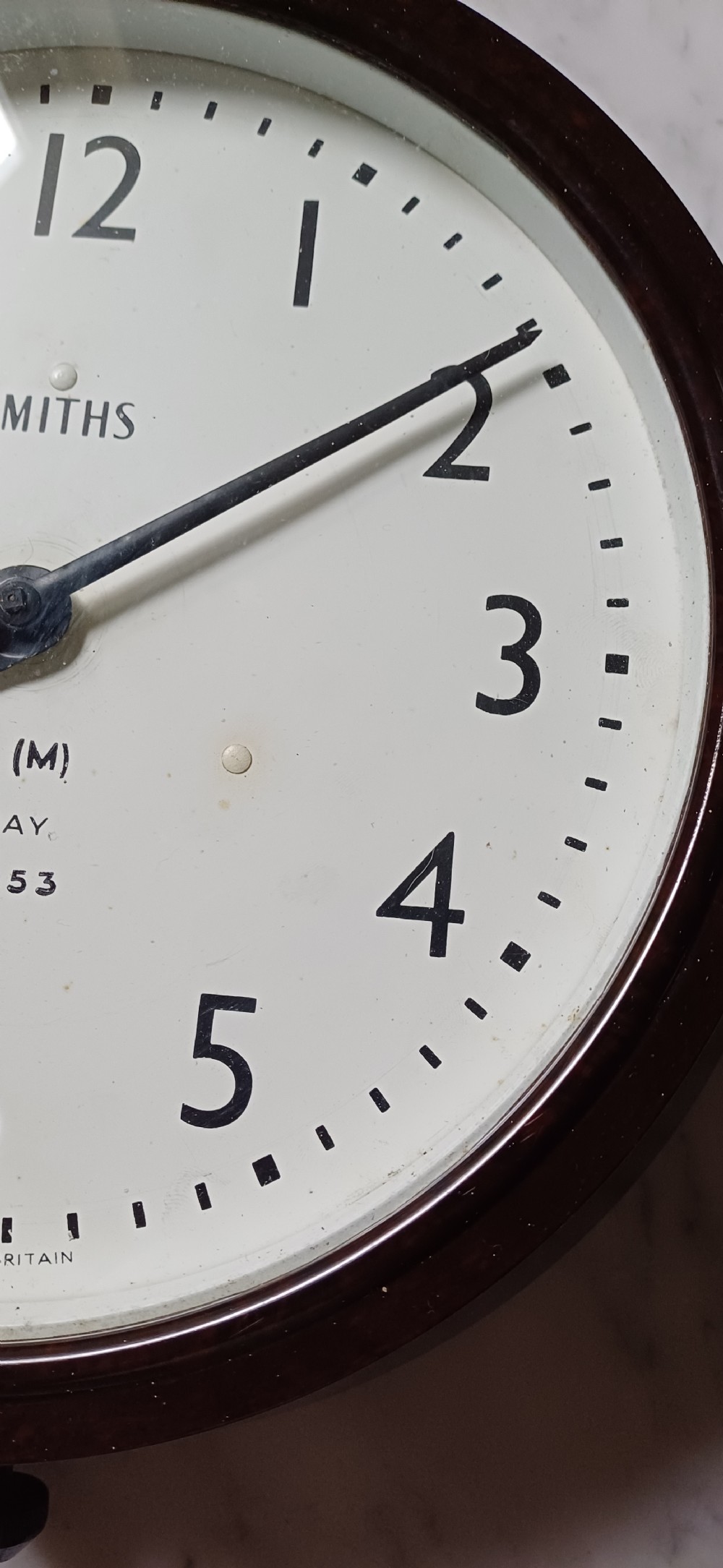 A circular mid-century wall clock featuring a moulded dark brown Bakelite case, a white dial with black Arabic numerals, and dark hands. View XIII
