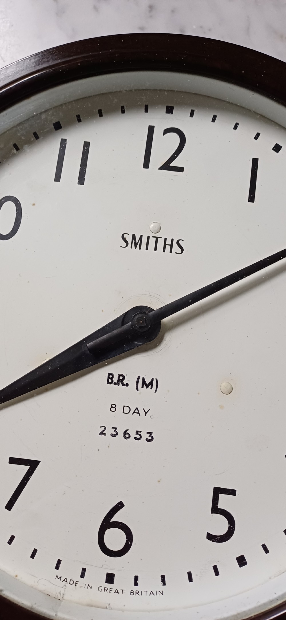 A circular mid-century wall clock featuring a moulded dark brown Bakelite case, a white dial with black Arabic numerals, and dark hands. View XIV