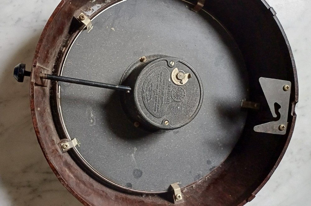 A circular mid-century wall clock featuring a moulded dark brown Bakelite case, a white dial with black Arabic numerals, and dark hands. View XV
