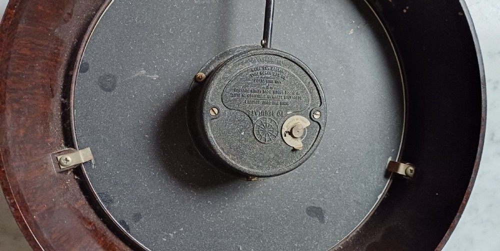 A circular mid-century wall clock featuring a moulded dark brown Bakelite case, a white dial with black Arabic numerals, and dark hands. View XVI