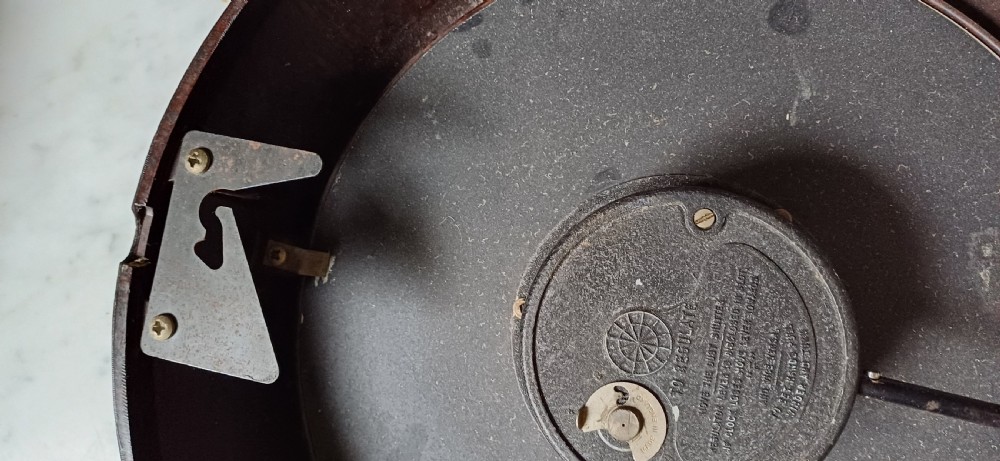 A circular mid-century wall clock featuring a moulded dark brown Bakelite case, a white dial with black Arabic numerals, and dark hands. View XVII