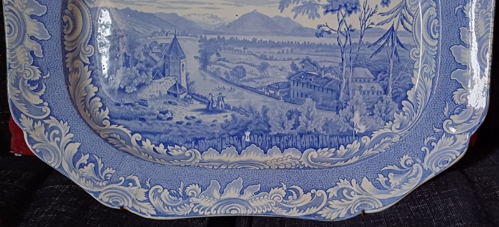 A large oval blue and white earthenware serving platter featuring an underglaze transfer-printed landscape scene framed by an ornate scroll border. View III