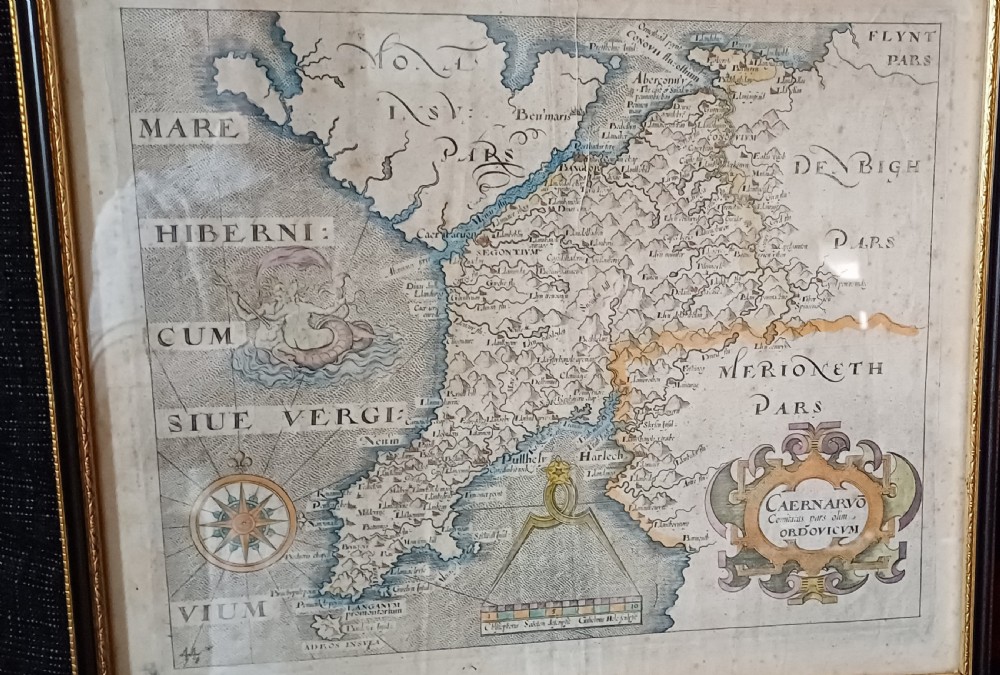 A framed 17th-century hand-coloured map of Caernarvonshire featuring a decorative cartouche, compass rose, and sea monster illustration. View IV