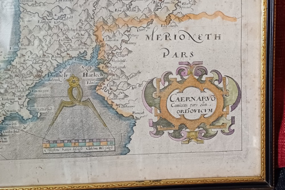 A framed 17th-century hand-coloured map of Caernarvonshire featuring a decorative cartouche, compass rose, and sea monster illustration. View VII