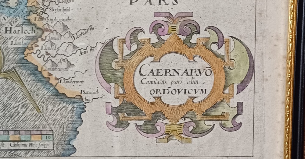 A framed 17th-century hand-coloured map of Caernarvonshire featuring a decorative cartouche, compass rose, and sea monster illustration. View XI
