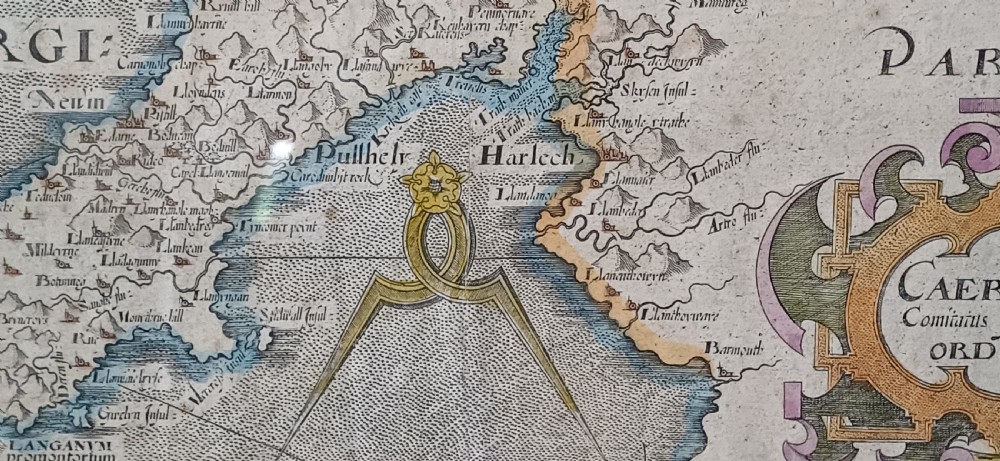 A framed 17th-century hand-coloured map of Caernarvonshire featuring a decorative cartouche, compass rose, and sea monster illustration. View XII