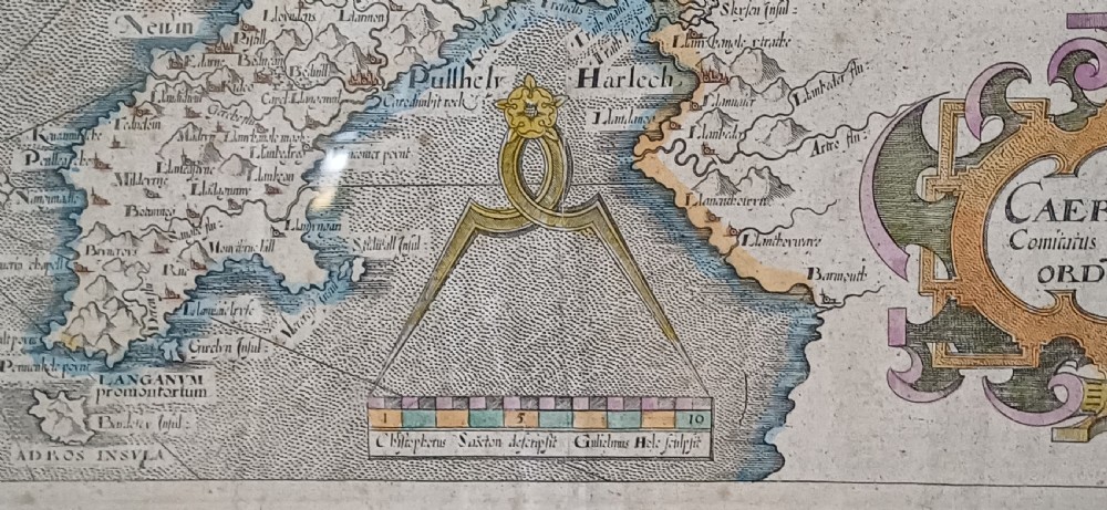 A framed 17th-century hand-coloured map of Caernarvonshire featuring a decorative cartouche, compass rose, and sea monster illustration. View XIV