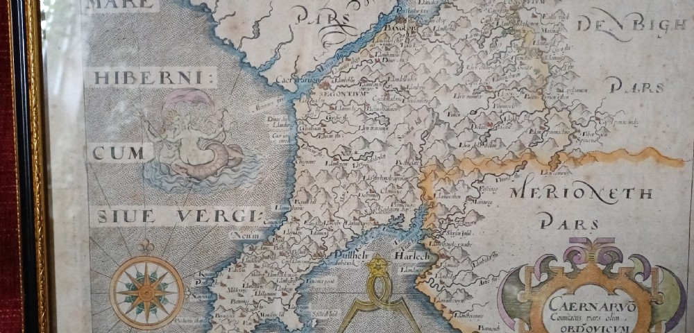 A framed 17th-century hand-coloured map of Caernarvonshire featuring a decorative cartouche, compass rose, and sea monster illustration. View XV