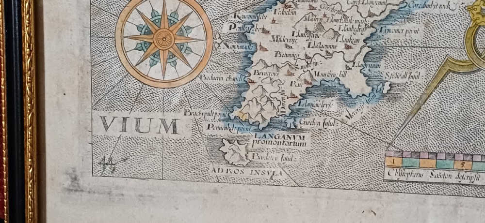A framed 17th-century hand-coloured map of Caernarvonshire featuring a decorative cartouche, compass rose, and sea monster illustration. View XVI