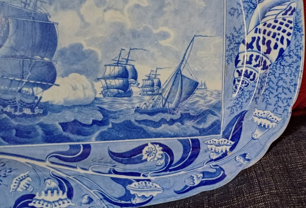 An oval blue and white earthenware transferware platter featuring a central naval sea battle scene surrounded by a botanical and seashell border. View VIII