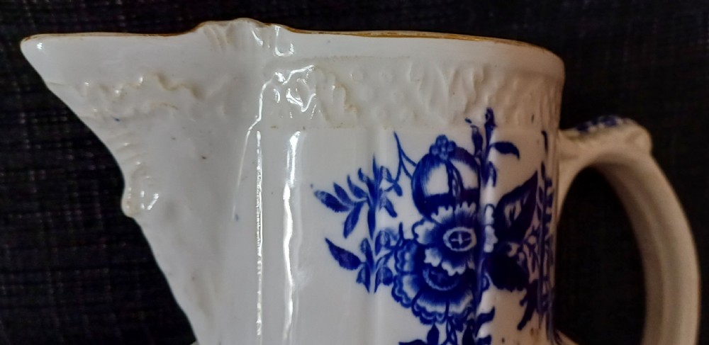 A Georgian porcelain jug featuring blue transferware floral and pine cone patterns with a moulded mask spout and ribbed body. View X