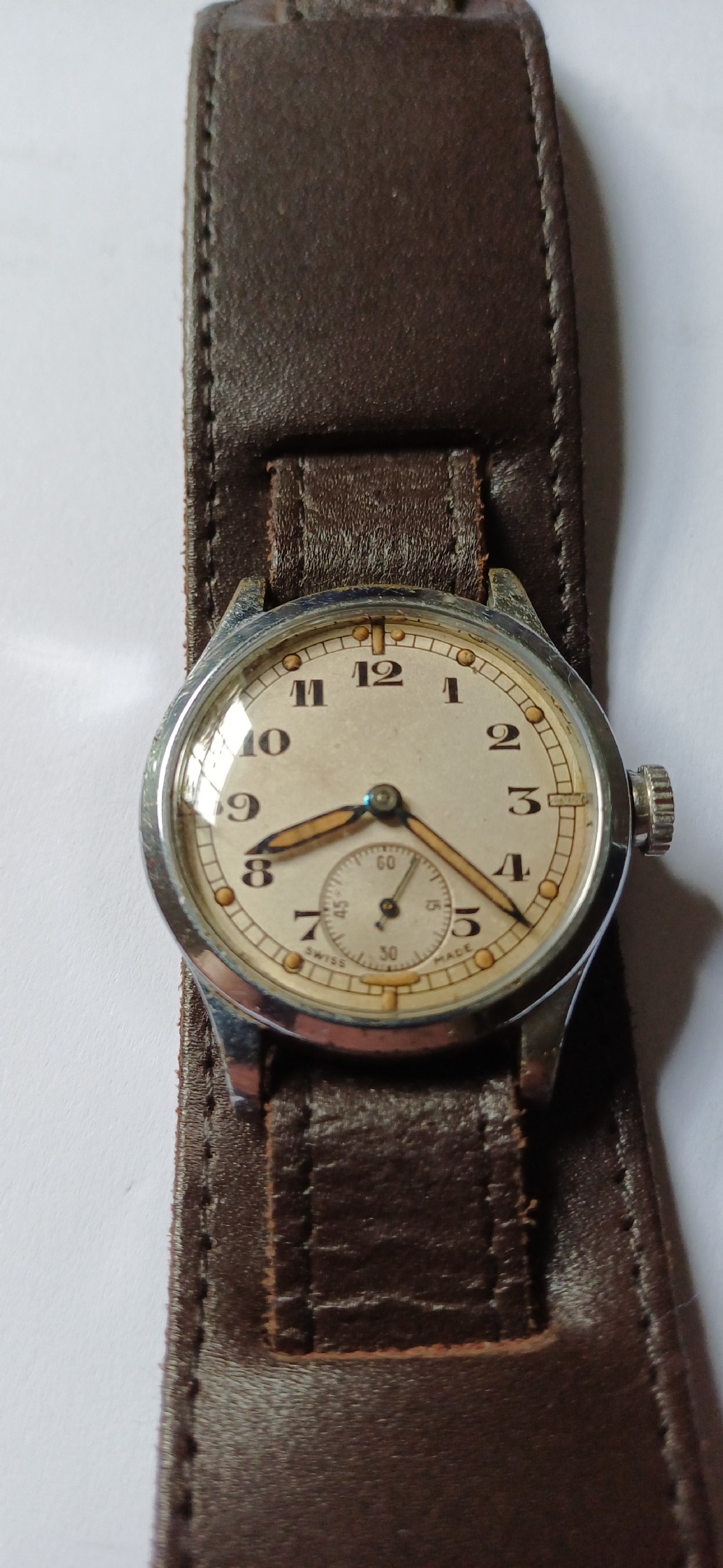 A vintage 1940s military wristwatch with a cream dial, Arabic numerals, sub-seconds display, and a wide brown leather cuff strap. View II
