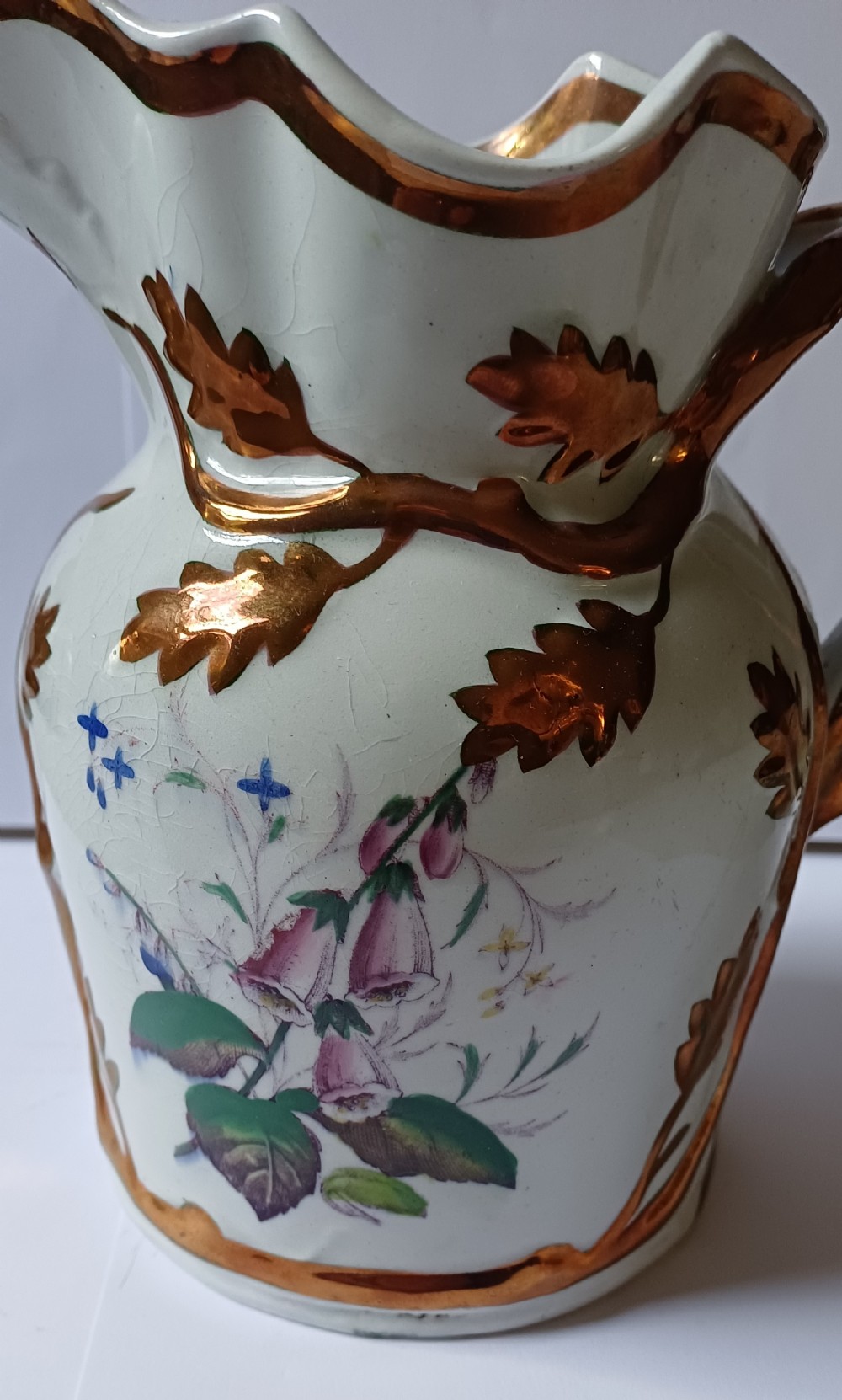An antique off-white ironstone jug decorated with copper lustre relief leaves around the rim and handle, featuring painted botanical flowers on the body. View II