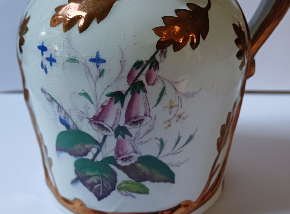 An antique off-white ironstone jug decorated with copper lustre relief leaves around the rim and handle, featuring painted botanical flowers on the body. View XIII